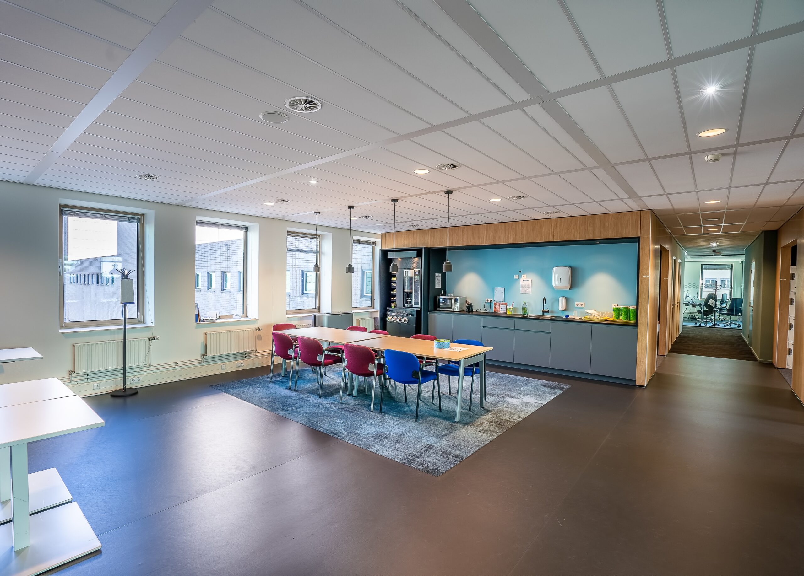 Interior of the kitchen area of a modern office with a long wooden table and chairs